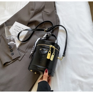 Detail of black cylindrical bucket bag with gold hardware and printed silk scarf handle