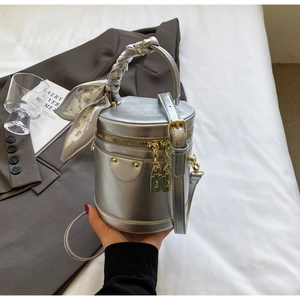 Detail of silver cylindrical bucket bag with decorative scarf on white bedding