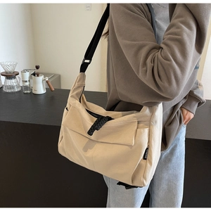 Detail of beige canvas crossbody bag with black adjustable strap and brand label