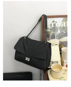 Détail d'un sac bandoulière en denim noir avec chaîne argentée et fermoir tournant en métal