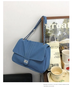 Détail du sac à bandoulière en denim bleu avec chaîne argentée et fermoir rotatif en métal