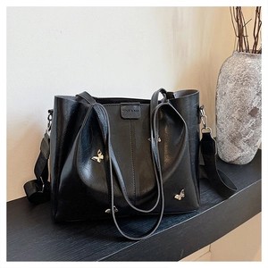 Close-up of black pleated tote bag featuring gold butterfly charms and wide woven strap