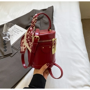 Detail of wine red bucket bag featuring a silk scarf handle and golden zipper accents