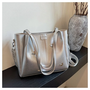 Detail of silver tote bag with metallic crinkled texture, butterfly buckle, and wide strap