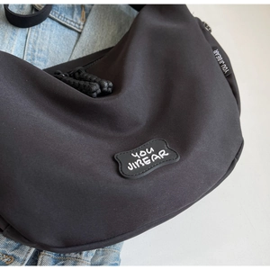 Gros plan sur le sac bandoulière en nylon noir avec logo You Ji Bear et fermeture éclair