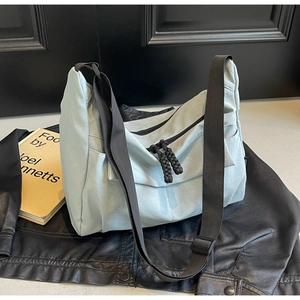 Detail view of light blue canvas crossbody bag with adjustable black strap and woven zipper pull