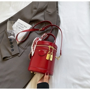 Detail of red bucket bag featuring gold lock zippers and decorative silk scarf handle