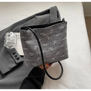 Détail du sac en toile grise avec broderie de nœuds blancs et breloque argentée