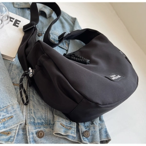 Gros plan d'un sac besace noir en forme de croissant sur une veste en jean