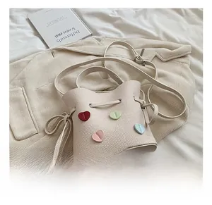 Gros plan du sac seau en cuir beige avec cœurs 3D colorés et fermeture à cordon