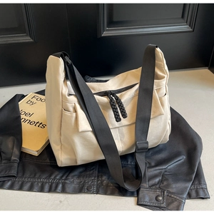Detail of cream canvas crossbody bag with adjustable black strap on leather jacket