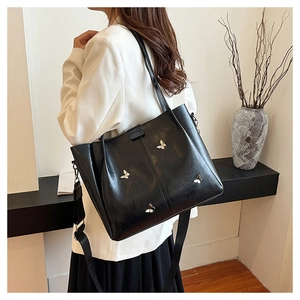Detail of black leather tote bag featuring silver butterfly accents and wide shoulder strap