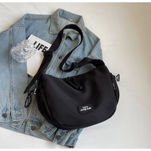 Mise à plat d'un sac demi-lune minimaliste en toile noire sur veste en jean bleu