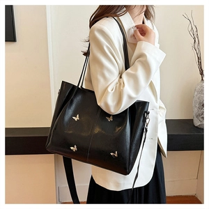 Detail of black leather tote bag with golden metal butterfly charms and dual strap options