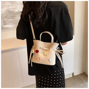 Détail du sac seau blanc cassé avec écussons cœur et texture en similicuir grainé