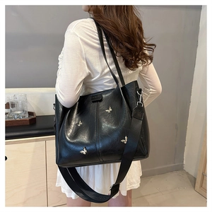 Detail view of black tote bag with silver butterfly charms and dual shoulder straps