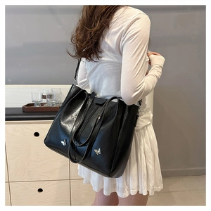 Detail of black leather tote bag featuring a silver butterfly buckle decoration on strap