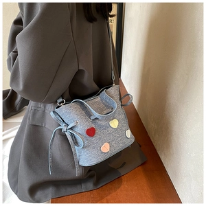 Vue détaillée du sac seau en denim bleu avec des patchs de cœur colorés et cordon serrage