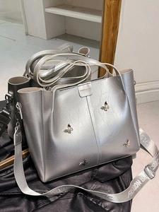 Silver crackle texture tote bag with metal butterfly and wide fashion strap on black surface
