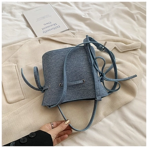 Détail du sac seau en denim bleu avec fermeture à cordon et nœud sur fond de velours