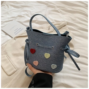 Détail du sac seau en denim bleu avec écussons cœurs colorés et fermeture à cordon