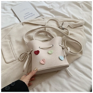 Détail du sac seau crème montrant la texture litchi et les appliques en forme de cœur