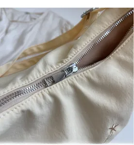 Dettaglio della cerniera argento e ricamo a stella su borsa a tracolla in nylon beige