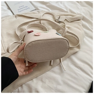 Détail du sac seau beige avec écussons cœurs en 3D et texture en cuir litchi grainé