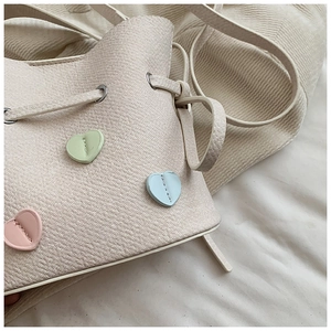 Gros plan du sac seau en sergé beige avec écussons cœur pastels et œillets métalliques