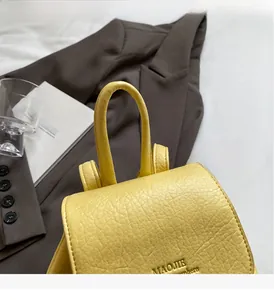 Detail of yellow pebbled leather backpack showing the comfortable round top handle and flap