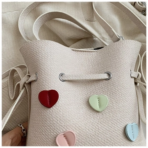 Gros plan d'un sac seau crème à texture litchi avec appliques de cœurs colorés cousus