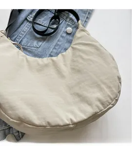 Detail of soft beige nylon dumpling bag with black strap on denim background