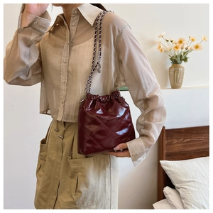 Detail of burgundy quilted bucket bag with chain strap shown in a cozy home interior