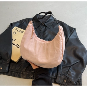 Detail of light pink nylon crescent bag with adjustable black strap on a leather jacket