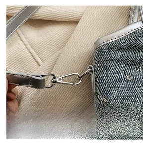 Détail du crochet en métal argenté et des rivets sur un sac cabas en denim bleu clair