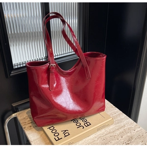 Close-up of deep red glossy leather tote bag with subtle texture on a marble surface