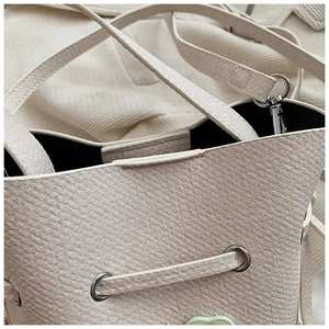 Détail du sac seau beige montrant la texture litchi et la décoration de coeur vert