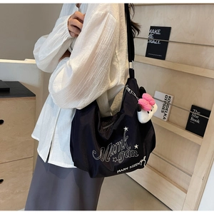 Dettaglio della borsa tote in nylon nero con tipografia bianca e ciondolo a peluche