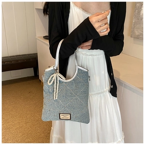 Détail du sac à main en jean bleu clair avec matelassage en losange et breloque en perles