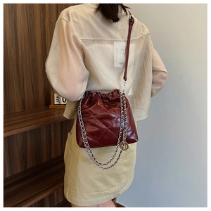 Detail view of burgundy quilted bucket bag with chain strap and metallic charms