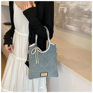 Détail du sac cabas en denim bleu clair avec nœud en perles et poignée argentée