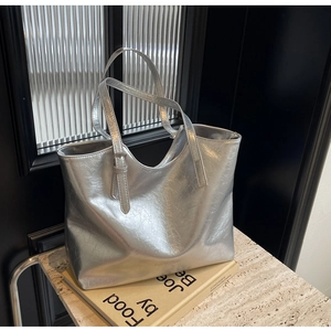 Detailed view of silver metallic tote bag with wrinkled texture on a stone surface