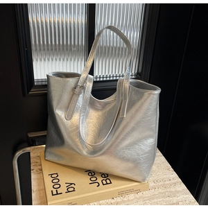 Detailed macro view of silver metallic tote bag featuring pleated texture and brand logo