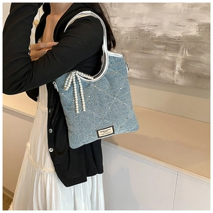 Détail du sac en jean bleu clair avec coutures en losange et breloque noeud en perles