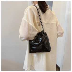 Close-up of black quilted bucket bag with chain strap worn over a white shirt