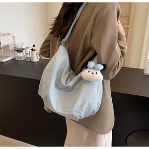 Dettaglio della borsa hobo in nylon celeste con ricamo bianco e portachiavi a forma di cane