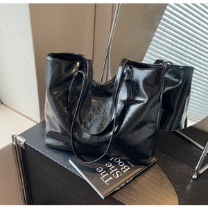 Detail of large black tote bag featuring glossy crinkle leather and dual shoulder straps