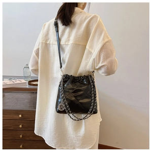 Detail of black quilted bucket bag with silver chain strap and metal charm on a model