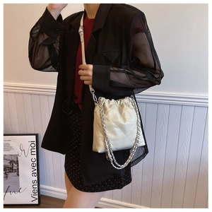Detail of cream quilted bucket bag with silver chain strap worn over a black blazer