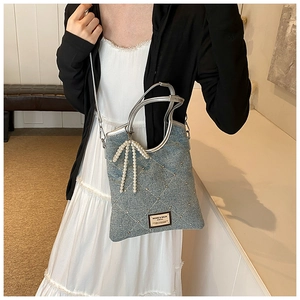 Détail d'un sac bandoulière en denim bleu clair avec nœud en perles et strass
